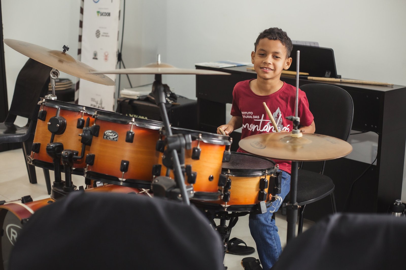 Menino sorrindo enquanto toca bateria na aula de música